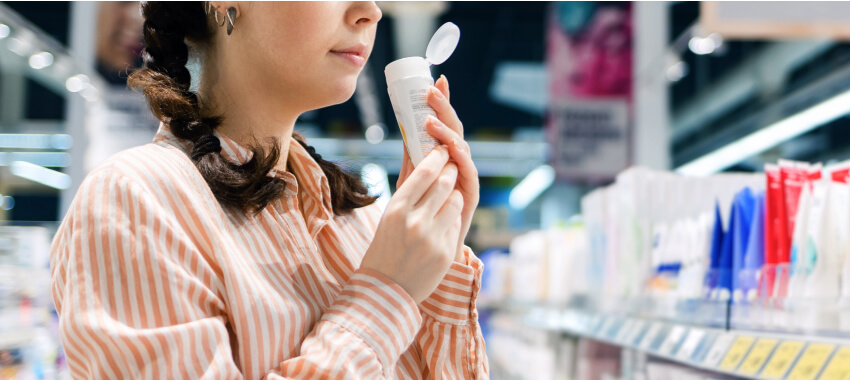 Woman in a peach and white striped shirt examining a white bottle or container while shopping in what appears to be a pharmacy or retail store.