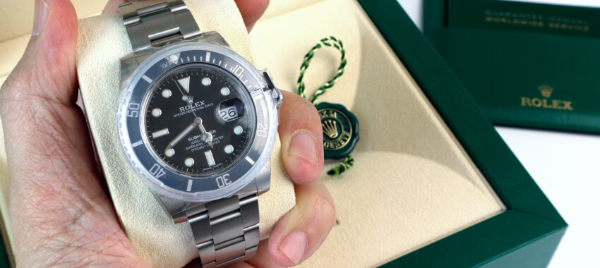 Hand holding stainless steel Rolex Submariner watch with green leather presentation box and documentation