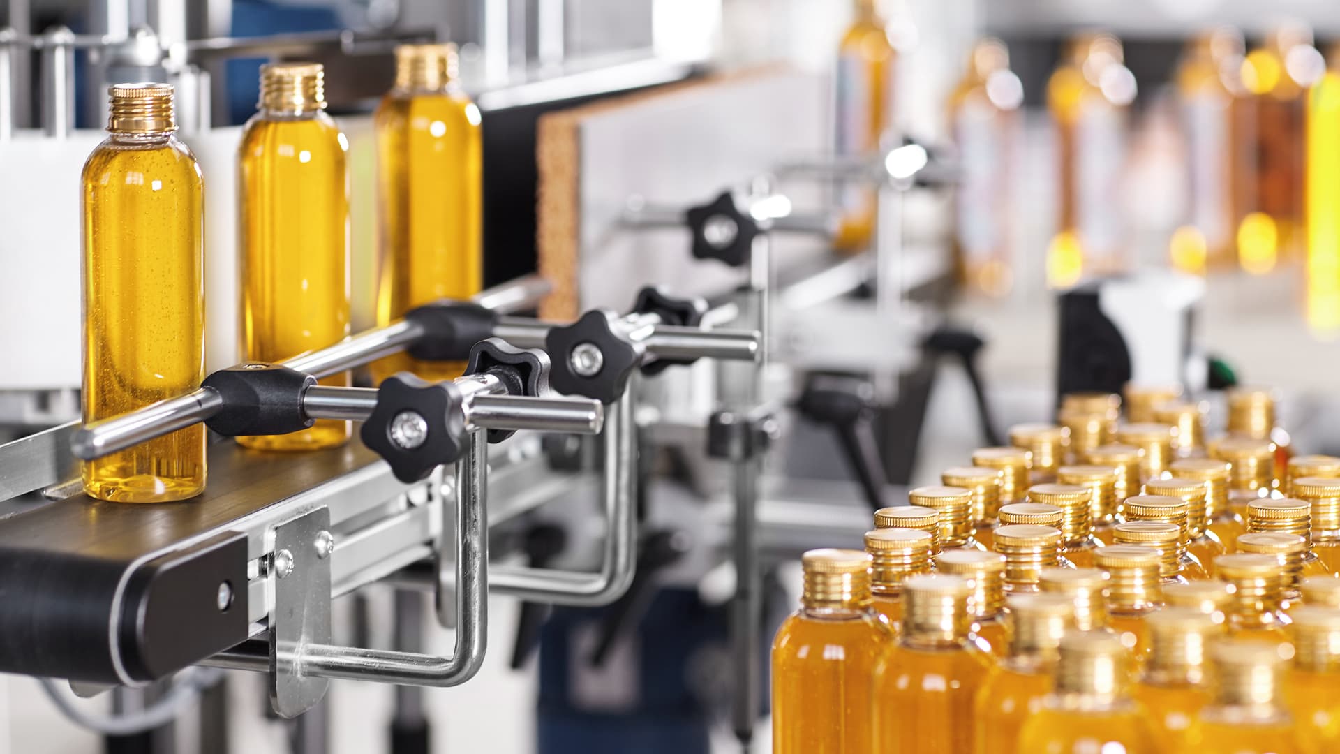 Amber-colored bottles with gold caps move along a factory conveyor belt during the cosmetics packaging process.
