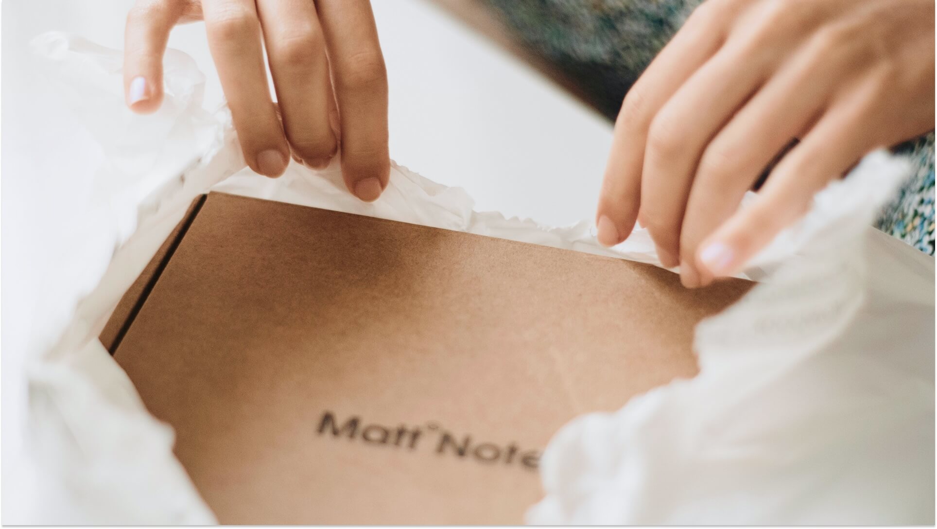 Hands opening branded cardboard mailer box with tissue paper revealing premium unboxing experience