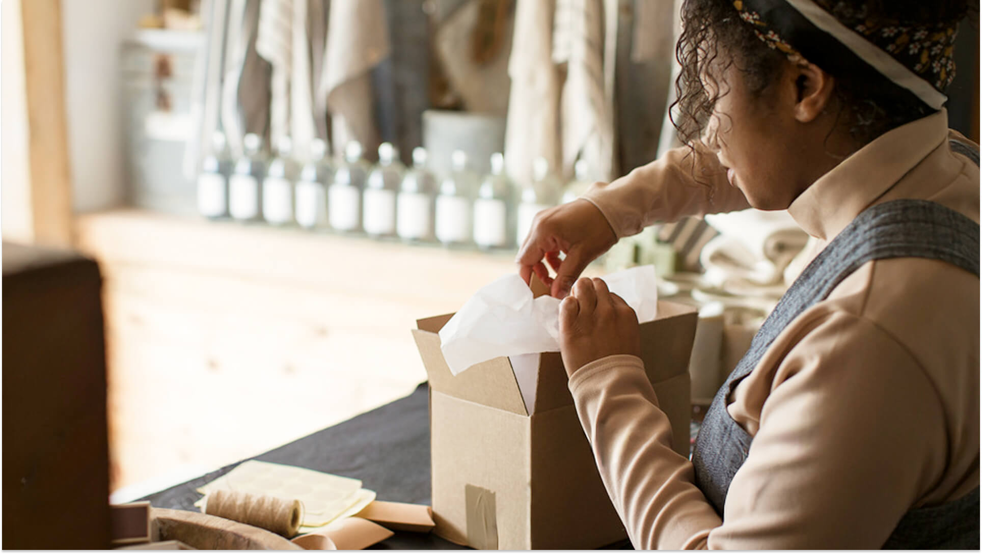 Small business owner carefully packing handmade product with tissue paper in craft box at artisan workshop