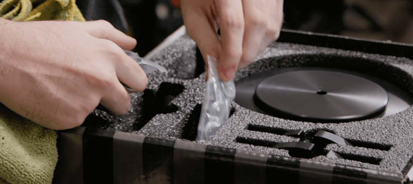 Hands placing or removing a vaping device from a black protective case with custom foam cutouts designed to hold the device and accessories.